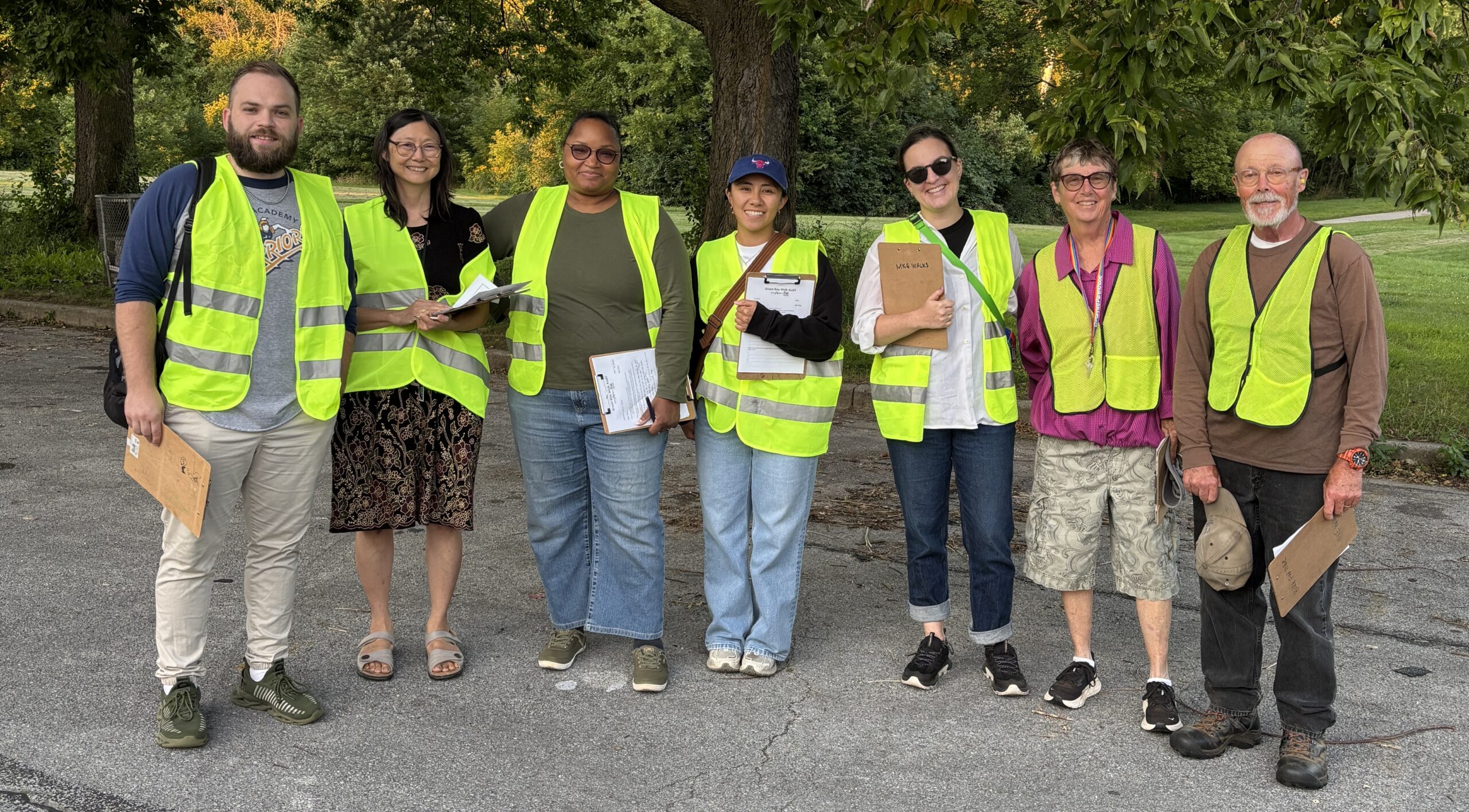 A group of people wearing hi-viz vests, smiling at the camera and holding clipboards